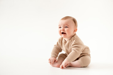 Fototapeta premium a crying baby on an isolated white background, a small boy crying or calling for his mother in a brown knitted suit