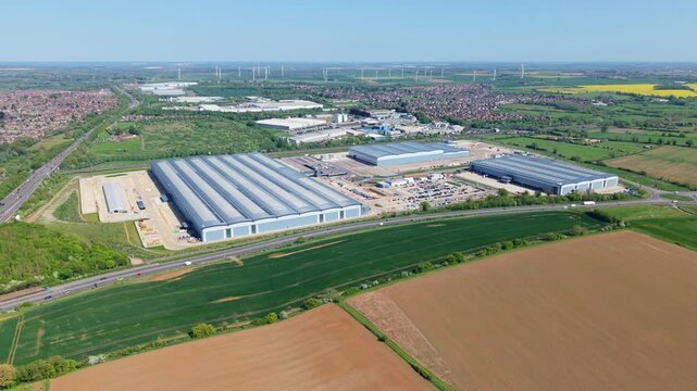 High angle drone tracking shot across a sprawling commercial fulfillment center in Northamptonshire