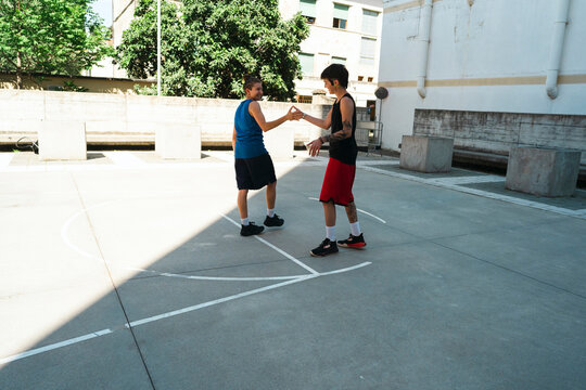 Two young men face each other on an outdoor court, hands raised in a gesture of interaction. They are preparing for a game or activity on a sunny day.