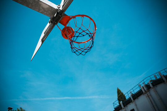 A basketball descends through an outdoor hoop, its net featuring red, white, and blue colors, set against a vibrant clear blue sky on a bright day.