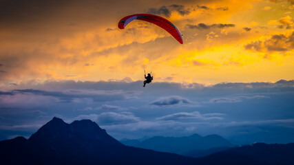 Paraglider silhouette soaring above mountain range at dramatic golden sunset © Nils