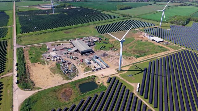 Close up aerial view of a wind turbine and solar panel array co-located with a battery energy storage system (BESS), UK.