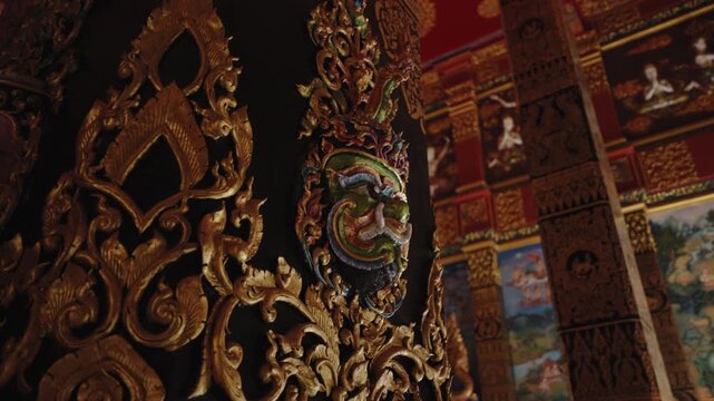 Detailed View of Yaksha Guardian Mask on Ornate Pillar, Golden Bas-relief against Background of Vibrant Sacred Murals inside Wat Bang Thong Pagoda