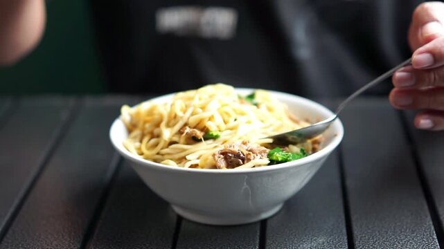 Asian is eating mie ayam (Indonesian noodle). Noodle with minced chicken with boiled mustard greens