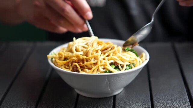 Asian is eating mie ayam (Indonesian noodle). Noodle with minced chicken with boiled mustard greens