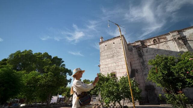Mature woman explores the Mission Church in San Ignacio Baja California Mexico and captures memories with her camera on a sunny day.