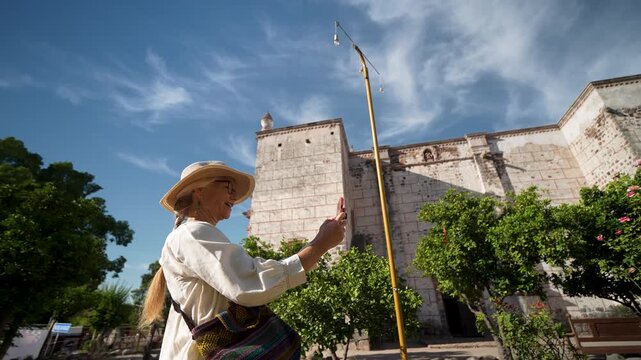 Mature woman takes photos while sightseeing at Mission Church in San Ignacio Baja California Mexico on a sunny day enjoying her trip.