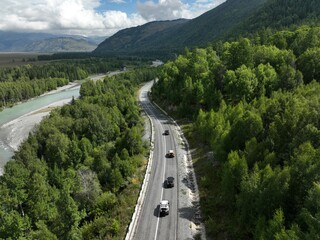 Obraz premium Aerial view of vehicles traveling along winding mountain road beside river