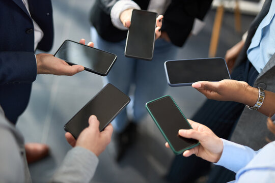 Close up of group of business people holding smartphones in a circle, high angle view.