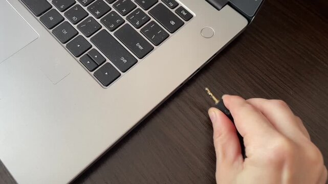 Disconnecting audio jack. Removing headphone plug carefully. Gently pulling audio connector out from port. Demonstration of unplugging headset connector from laptop port with careful handling