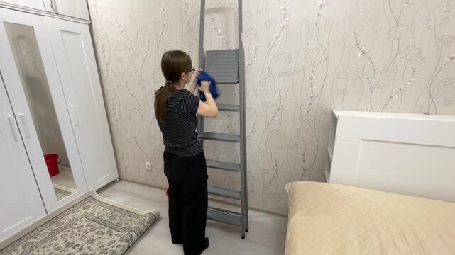 Person preparing for ceiling cleaning activity. Individual patiently setting up ladder and cleaning supplies. Woman systematically arranging ladder and tools for high cleaning chores in bedroom