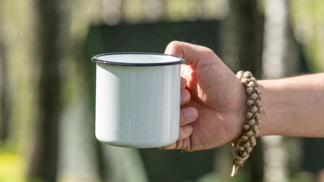 Man holding white enamel mug during camping in forest, close up