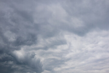 Mixed cloudscape with dark brooding storm clouds contrasting against lighter striated cloud layers across a grey sky © Philip