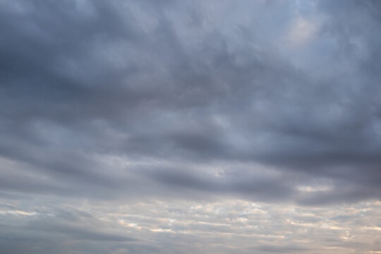 Layered cloudscape with dark stratus clouds sweeping across a blue-grey sky above a pale luminous horizon band