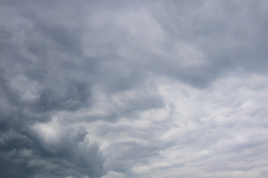 Mixed cloudscape with dark brooding storm clouds contrasting against lighter striated cloud layers across a grey sky