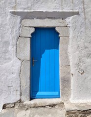 Fototapeta premium Photo of a traditional cobalt-blue wooden door set into a sunlit whitewashed wall, capturing a charming Cycladic architectural detail on Mykonos Island, Greece.