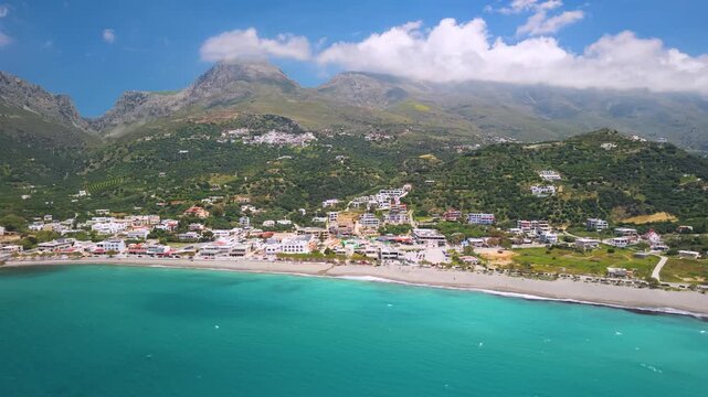Plakias South Crete Greece aerial view of Long Beach and white town, high mountains coastline drone parallel flight, Mediterranean seaside panoramic travel footage for vacation background