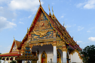 Fototapeta premium The magnificent facade of Wat Mongkol Nimit in Phuket Town. The golden pediment of this Buddhist temple features a majestic Garuda and intricate Thai motifs, framed by white pillars.
