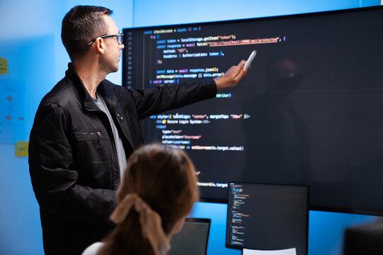 Software developers discussing code on large screen in office