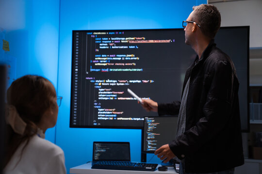 Software developers discussing code on large screen in office
