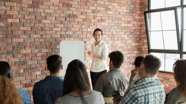 Businesswoman speaking at crowdsourcing seminar at loft office, pointing at whiteboard, copy space