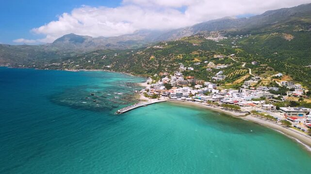 Aerial view of Plakias white village and long beach in South Crete, Greece. Drone reveal of turquoise sea, rugged coastline and distant mountains background. Cinematic flight to coastal town, 4k