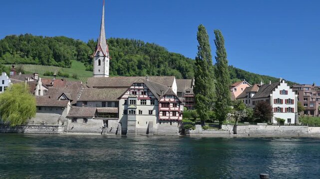 Scenic view across the Rhine to Stein am Rhein old town, Switzerland, with historic houses, riverside wall, and tall church spire on a sunny day.