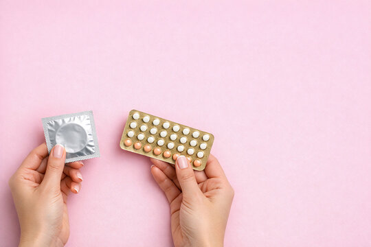 Close-up image of a person's hand displaying oral contraceptives and an intact condom against a blurred background. The focus is on the contrast between birth control methods.
