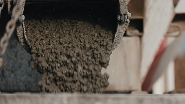 Pouring concrete from mixer chute into construction bucket close up