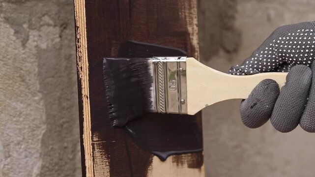 Process of wood coating with dark varnish. Handmade, do it yourself concept. Hand in protective glove holds brush, painting wooden surface. Close-up of female hand covering board with varnish