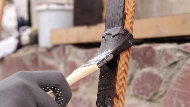 Process of wood coating with dark varnish. Handmade, do it yourself concept. Hand in protective glove holds brush, painting wooden surface. Close-up of female hand covering board with varnish