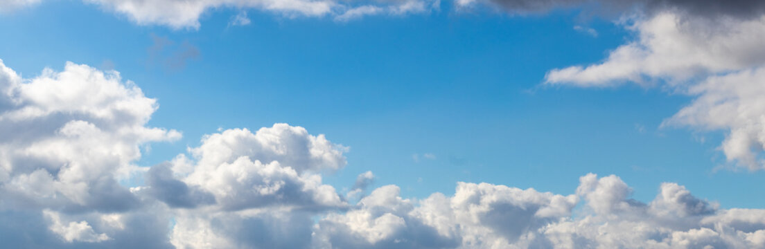Bright blue sky with white and dark grey clouds of various shapes, scenic wide format cloudscape shot