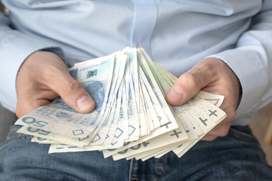 A businessman in a light shirt holds Polish money in his hand.
