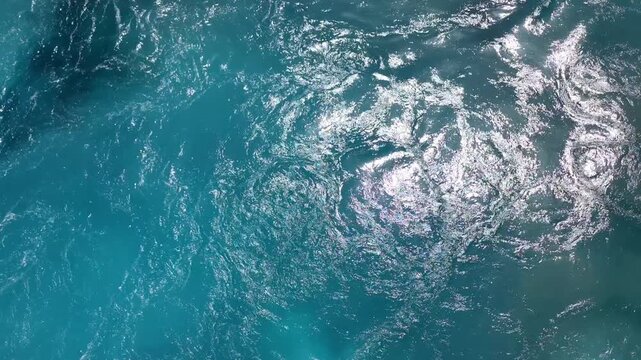 View of deep tonal layers of white sea foam and translucent turquoise wake swirling in the Aegean sea in Greece, creating a dynamic abstract seascape of motion and light.