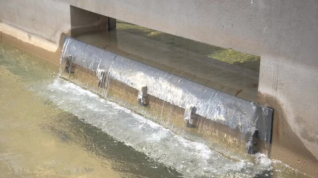 Close-up of clear water flowing over a stainless steel weir gate in a concrete water treatment basin. Perfect B-roll for water purification, environmental engineering, and municipal infrastructure.