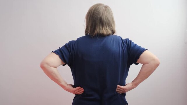An elderly woman stretching her sore lower back, seen from behind