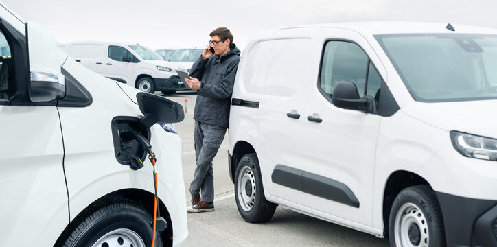 Fleet manager with digital tablet and smartphone supervising rows of white electric delivery vans
