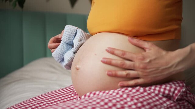 Young expectant couple expressing affection and excitement for their unborn child, with the mother holding tiny blue booties and the father gently stroking her pregnant belly