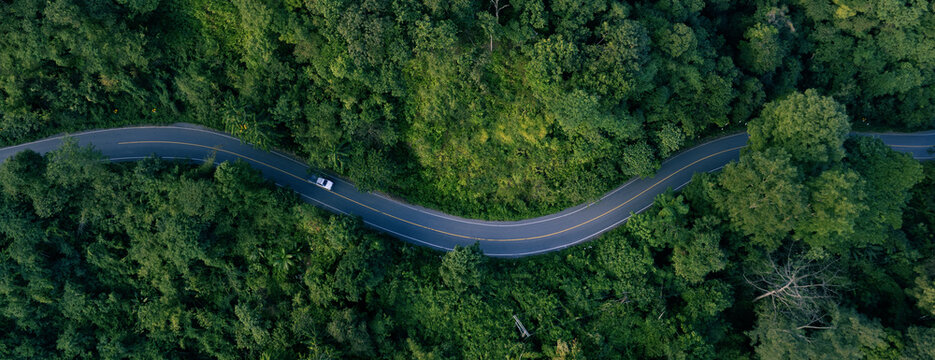 Aerial forest landscape with winding road and vehicles traveling through nature. Concept for sustainable mobility, ESG investment, climate awareness, green transport and eco friendly development.