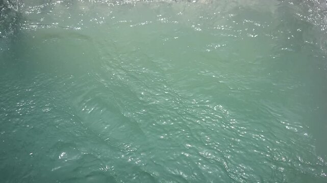 Top-down close-up of churning, swirling turquoise water. The vibrant teal surface features gentle ripples and subtle bubbling. Ideal abstract B-roll for fluid dynamics and nature backgrounds.