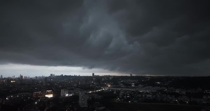 Wide angle night view of a massive shelf cloud advancing over a city skyline during a heavy monsoon storm.