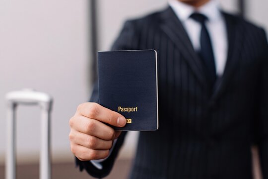 Businessman in a suit holding a blue passport, presenting it for international travel, business trip, or immigration