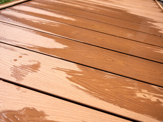 Fototapeta premium Wet WPC decking boards after rain near garden or pool. Modern composite terrace surface ideal for outdoor spaces, patios, poolsides and exterior design.