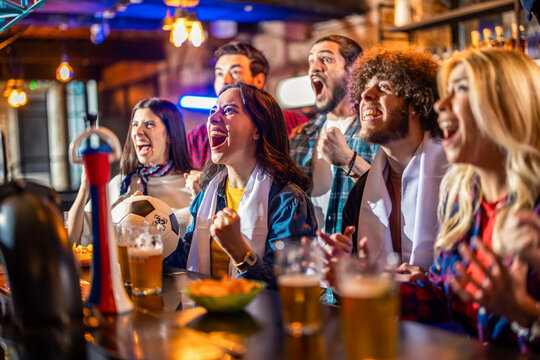Passionate fans with white scarves cheering for soccer goal in pub.