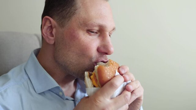 Caucasian male worker in office having fast food lunch at desk. Man eating hamburger while working in his office in front of the computer.