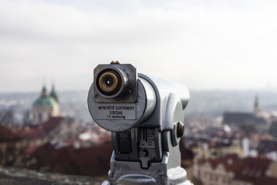 View of a tourist telescope overlooking the historic red rooftops and the green dome of St. Nicholas Church in Prague, Prague, Czechia.