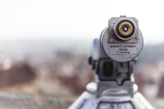 View of a tourist telescope eyepiece overlooking blurred historic rooftops and the city skyline in Prague, Prague, Czechia.