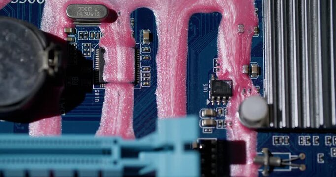 Circuit board. Ink trickles. Shimmering pink fluid pouring on blue motherboard texture. Color electronics system defocused background.