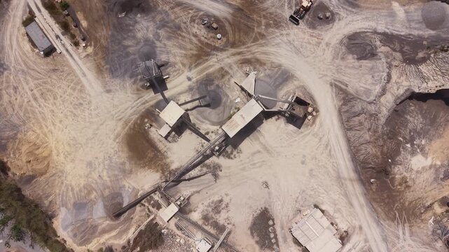 Overhead top-down perspective of an industrial gravel crushing and screening plant at an open pit sand quarry, with conveyor belts, machinery, and dirt access roads