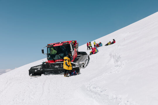 Group of mountaineers in colorful winter gear resting beside a snowcat on a steep snowy slope on Mount Elbrus, Kabardino-Balkaria, Russia, under clear blue sky